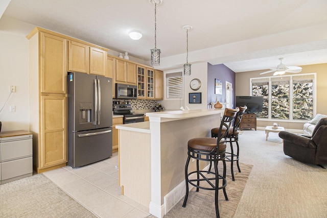 kitchen with glass insert cabinets, appliances with stainless steel finishes, open floor plan, a kitchen breakfast bar, and light brown cabinets