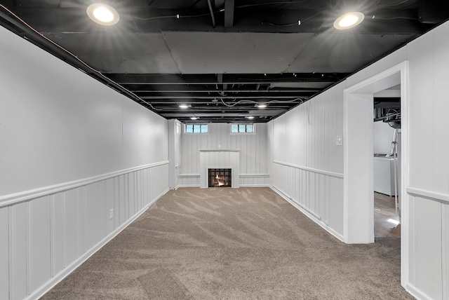 basement featuring a lit fireplace, washer / clothes dryer, and carpet flooring