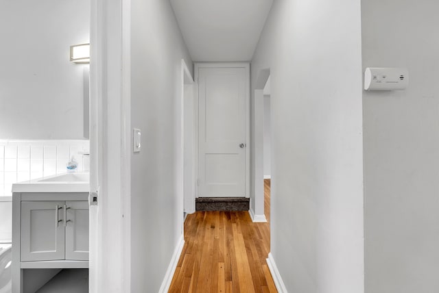 hall featuring baseboards, a sink, and light wood-style floors