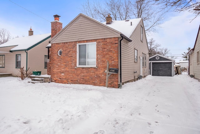 snow covered property featuring an outbuilding, brick siding, and a detached garage