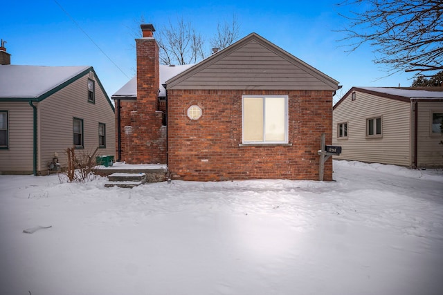 snow covered rear of property featuring brick siding and a chimney