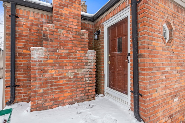 snow covered property entrance featuring brick siding