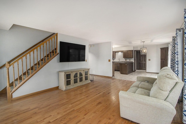 living room with stairs, baseboards, and light wood-style floors