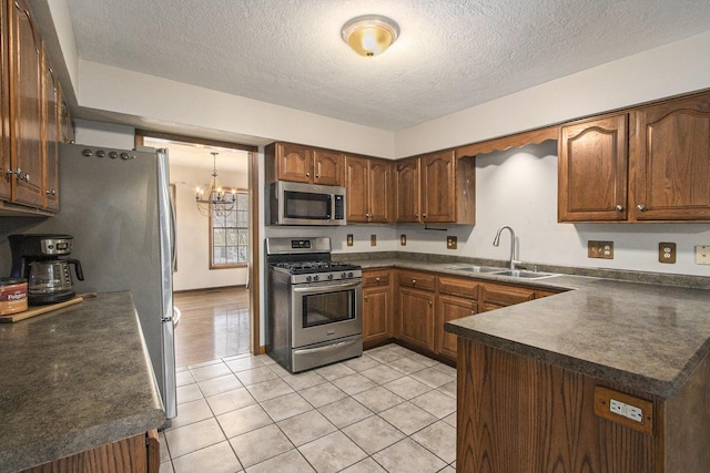 kitchen featuring light tile patterned flooring, a peninsula, a sink, appliances with stainless steel finishes, and dark countertops