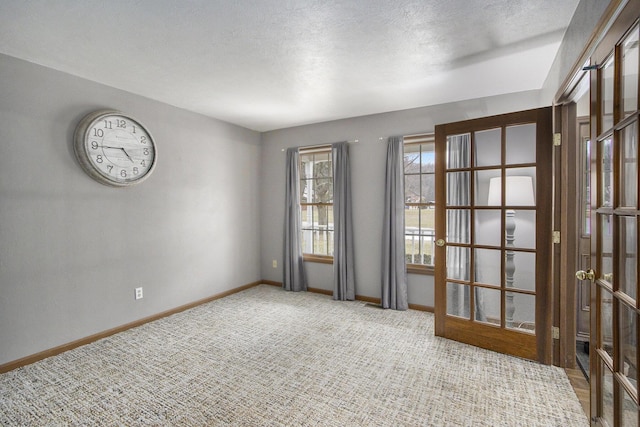 carpeted spare room featuring a textured ceiling, french doors, and baseboards