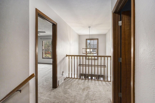 hallway with a textured wall, carpet, and a notable chandelier