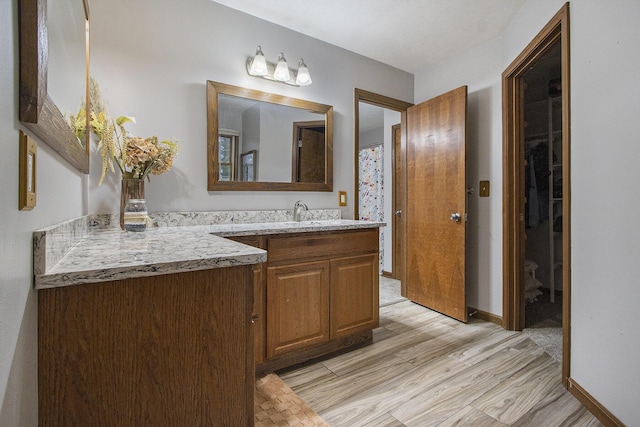 bathroom featuring a spacious closet, vanity, baseboards, and wood finished floors