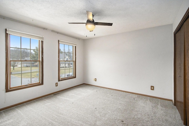 spare room with light colored carpet, ceiling fan, a textured ceiling, and baseboards