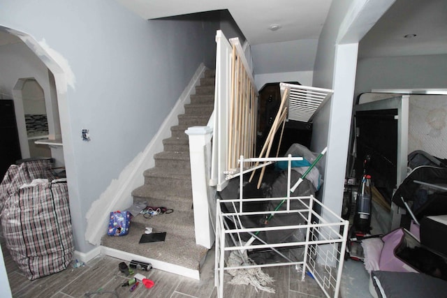 stairway featuring wood tiled floor, arched walkways, and baseboards