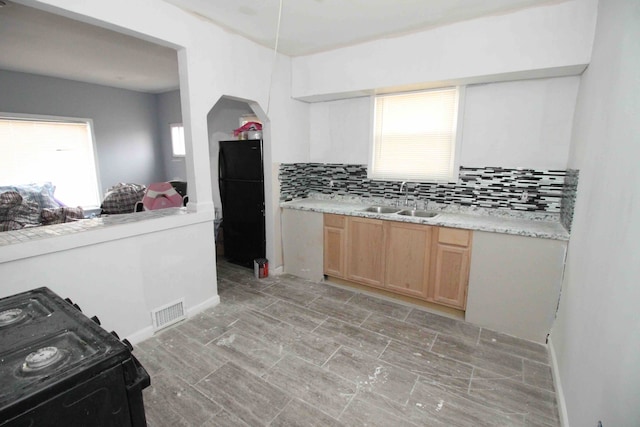 kitchen featuring arched walkways, tasteful backsplash, light countertops, light brown cabinets, and a sink