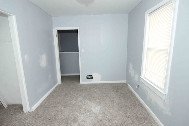 unfurnished bedroom with carpet floors, a walk in closet, a closet, and baseboards