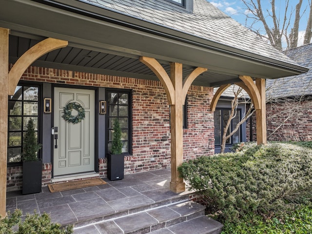 doorway to property with a porch, a high end roof, and brick siding