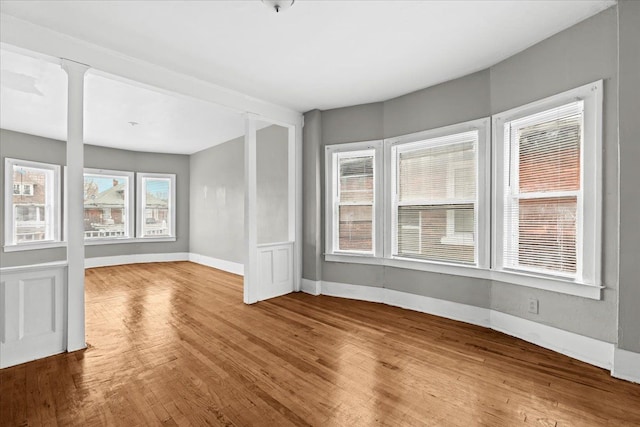 empty room featuring wood finished floors, decorative columns, and baseboards