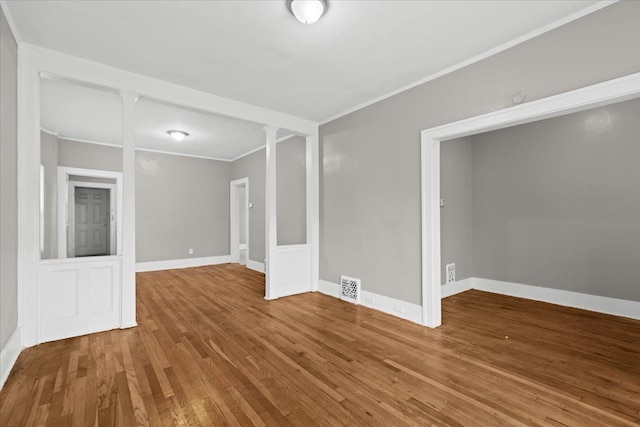 spare room featuring decorative columns, crown molding, visible vents, wood finished floors, and baseboards