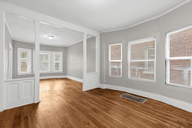 empty room featuring decorative columns, crown molding, visible vents, and wood finished floors