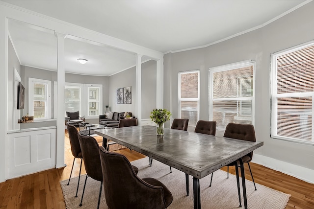 dining space featuring decorative columns, crown molding, baseboards, and wood finished floors