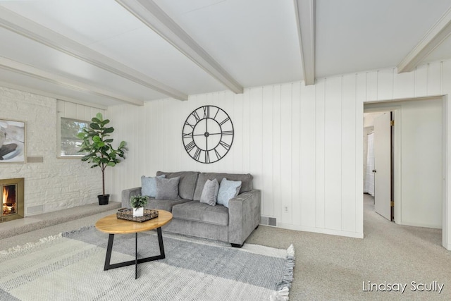 living area featuring carpet floors, visible vents, beam ceiling, and a stone fireplace