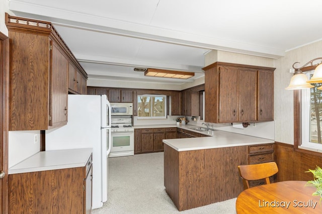 kitchen with a peninsula, white appliances, a sink, and light countertops