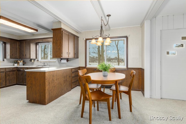 kitchen featuring a notable chandelier, a wainscoted wall, a peninsula, a sink, and light countertops