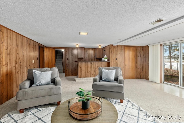 living room featuring a textured ceiling, light colored carpet, wood walls, visible vents, and stairway