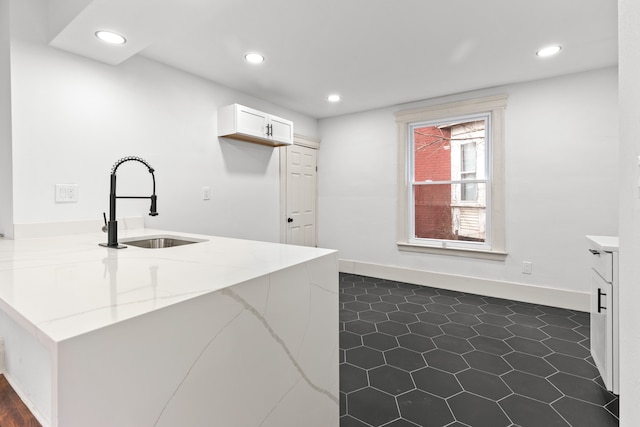 kitchen featuring baseboards, light stone countertops, white cabinetry, a sink, and recessed lighting