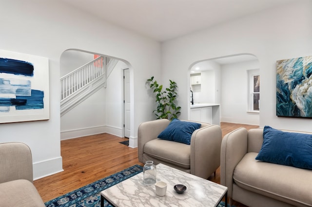 living room featuring light wood-type flooring, arched walkways, stairway, and baseboards