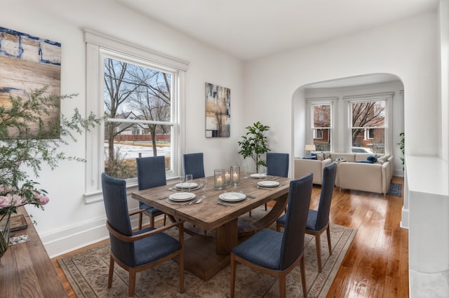 dining room featuring arched walkways, hardwood / wood-style floors, and baseboards