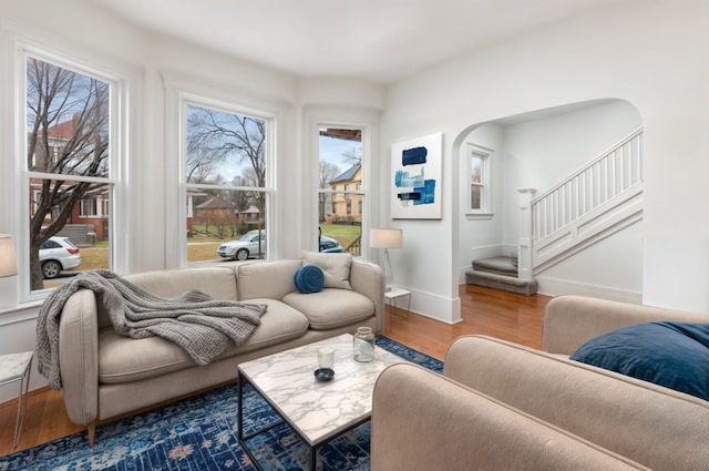 living area featuring stairs, baseboards, arched walkways, and wood finished floors