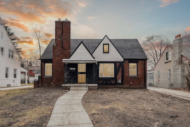 view of front of property with brick siding, fence, a chimney, and roof with shingles