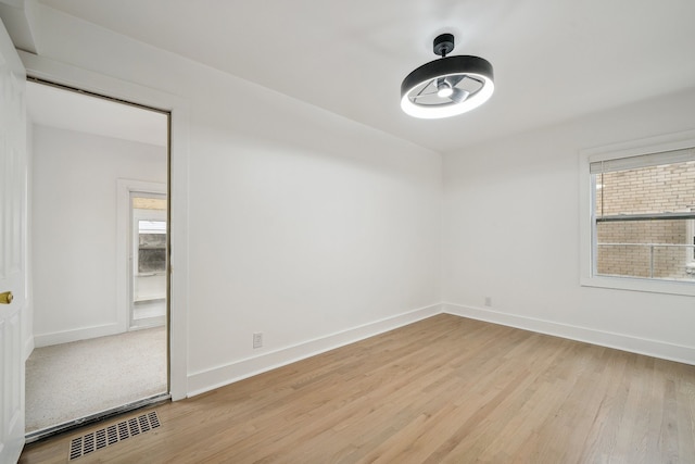 empty room featuring light wood-type flooring, a wealth of natural light, visible vents, and baseboards