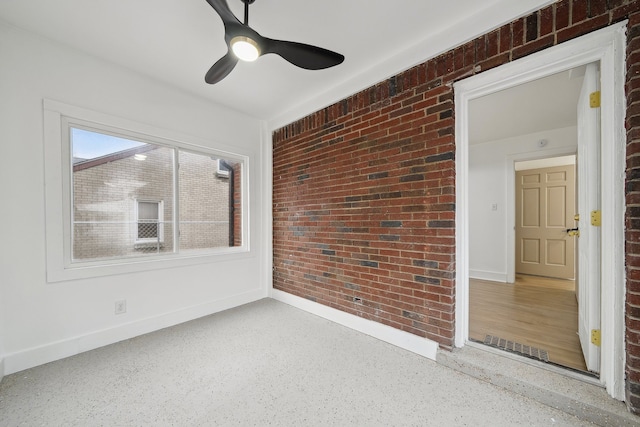 spare room featuring visible vents, ceiling fan, brick wall, baseboards, and speckled floor