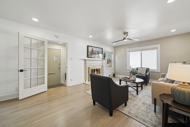 living room with baseboards, a glass covered fireplace, light wood-style flooring, ceiling fan, and recessed lighting