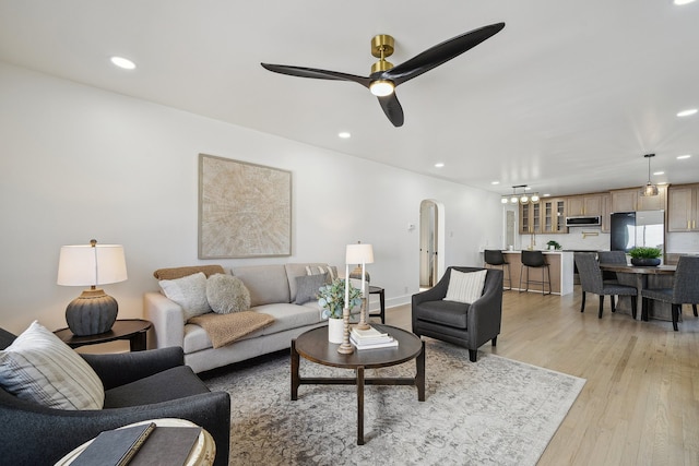 living room featuring light wood-style floors, arched walkways, a ceiling fan, and recessed lighting