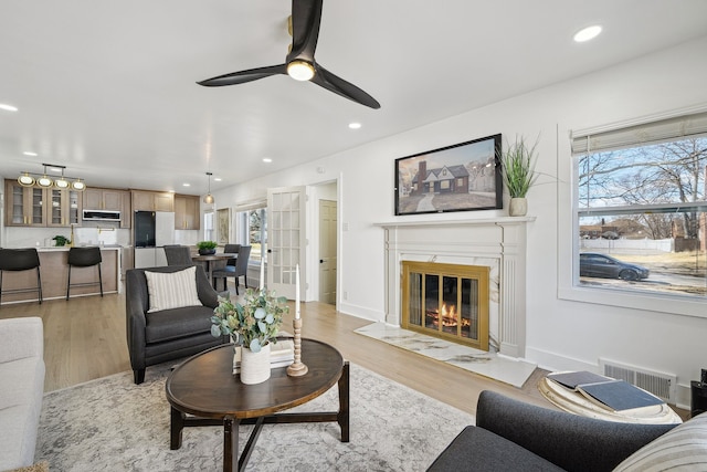 living room featuring recessed lighting, a high end fireplace, visible vents, and light wood-style floors