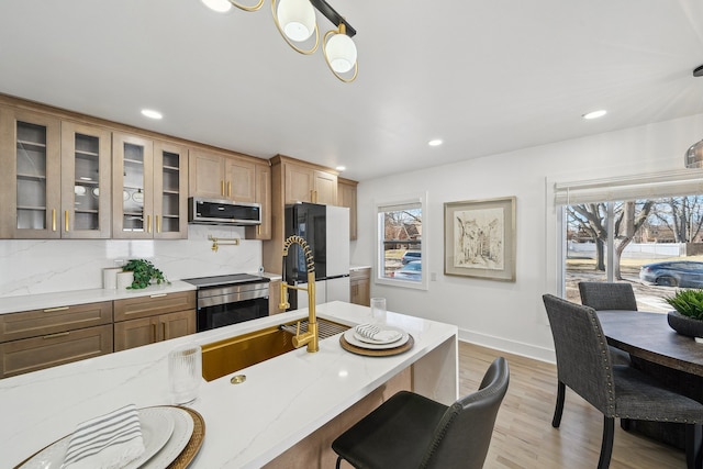 kitchen featuring light wood-style floors, freestanding refrigerator, decorative backsplash, stainless steel microwave, and glass insert cabinets