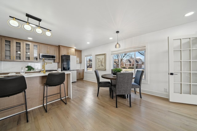 kitchen featuring a kitchen breakfast bar, light countertops, freestanding refrigerator, light wood finished floors, and stainless steel microwave