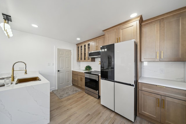 kitchen featuring light wood finished floors, appliances with stainless steel finishes, a sink, and decorative backsplash