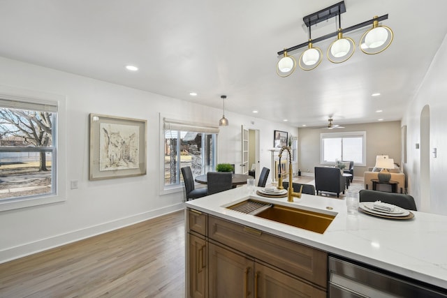 kitchen featuring light stone counters, light wood-style floors, pendant lighting, a sink, and recessed lighting