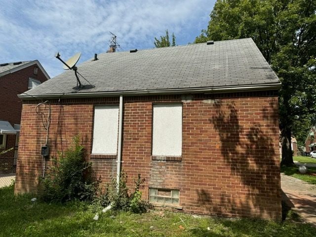 view of property exterior featuring brick siding and roof with shingles