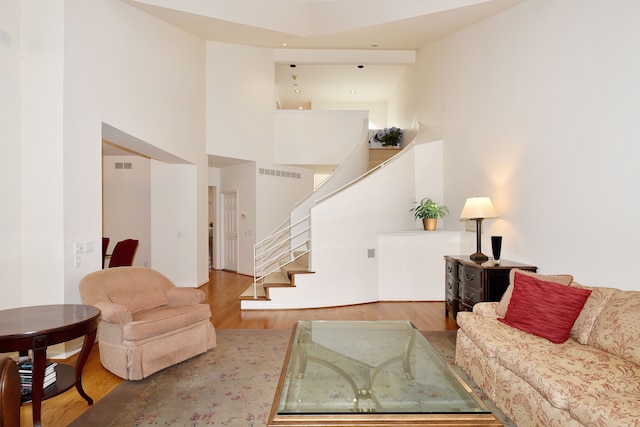 living area with stairs, visible vents, a towering ceiling, and wood finished floors