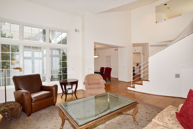 living area featuring a towering ceiling, visible vents, stairway, and wood finished floors