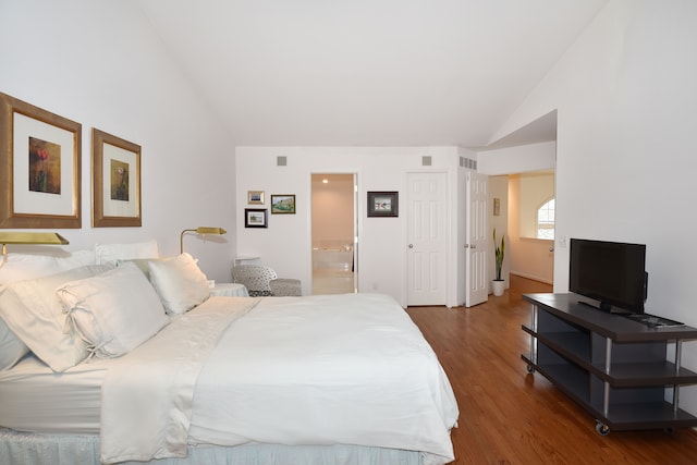 bedroom featuring lofted ceiling, visible vents, ensuite bathroom, and wood finished floors