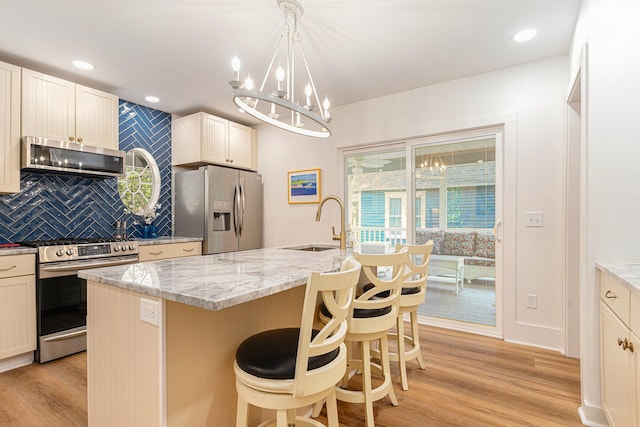 kitchen with light wood finished floors, light stone counters, a sink, stainless steel appliances, and backsplash