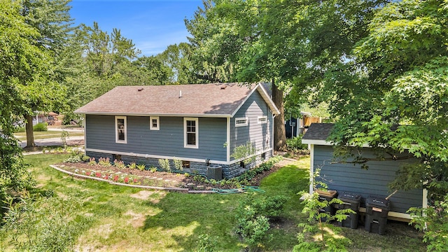 back of property with central air condition unit, a shingled roof, and a yard