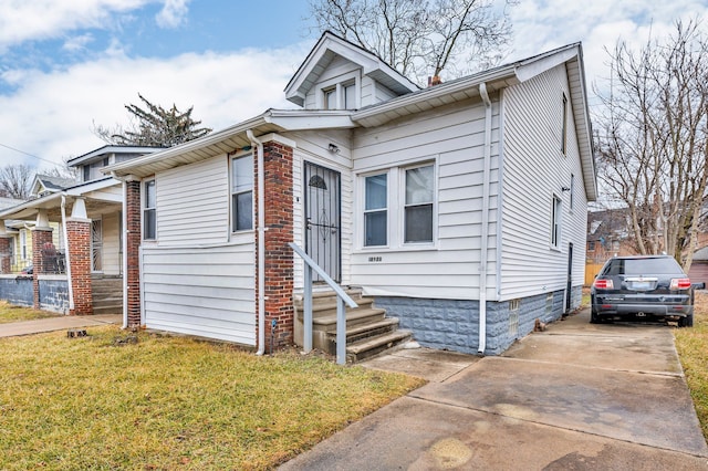 bungalow-style home with entry steps, concrete driveway, and a front yard