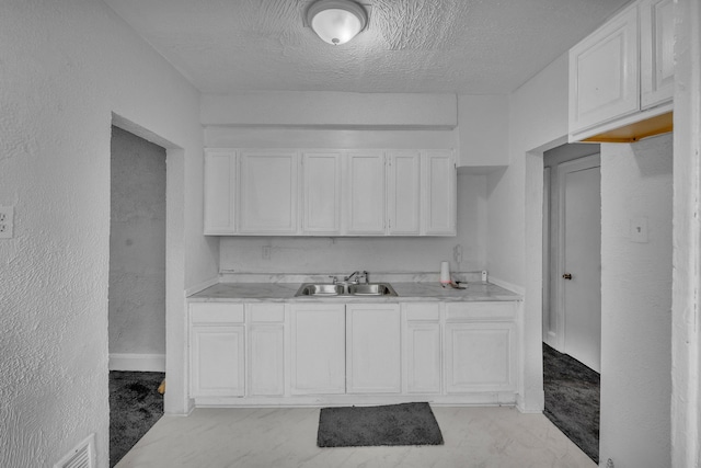 kitchen featuring a textured ceiling, a sink, visible vents, white cabinetry, and light countertops