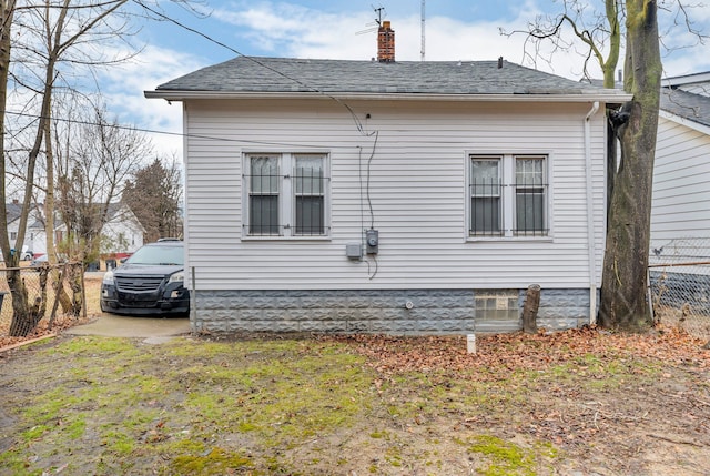 view of side of home with roof with shingles, fence, and a chimney