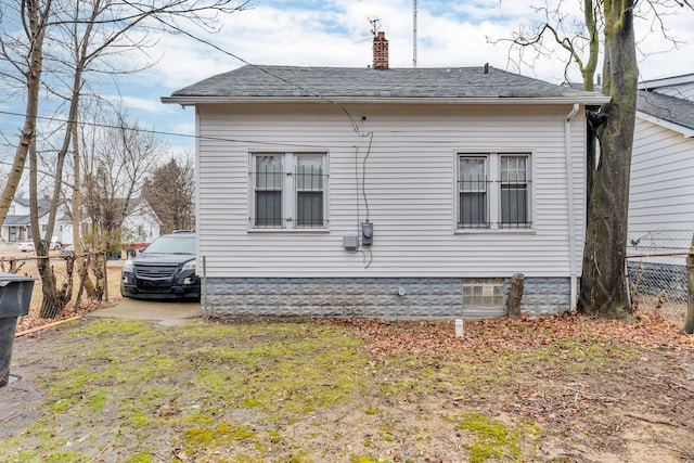 view of home's exterior with roof with shingles, fence, and a chimney