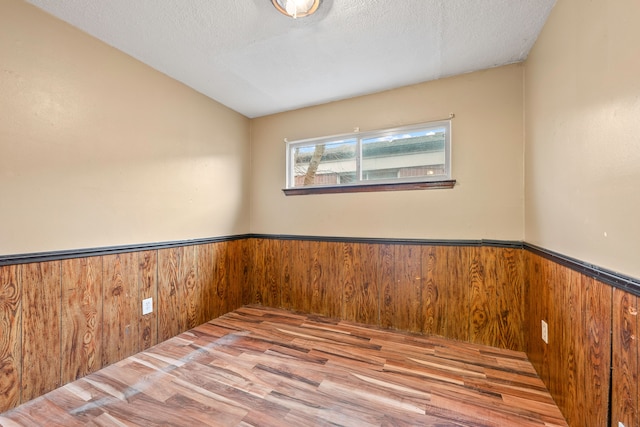 unfurnished room featuring a wainscoted wall, wooden walls, and a textured ceiling