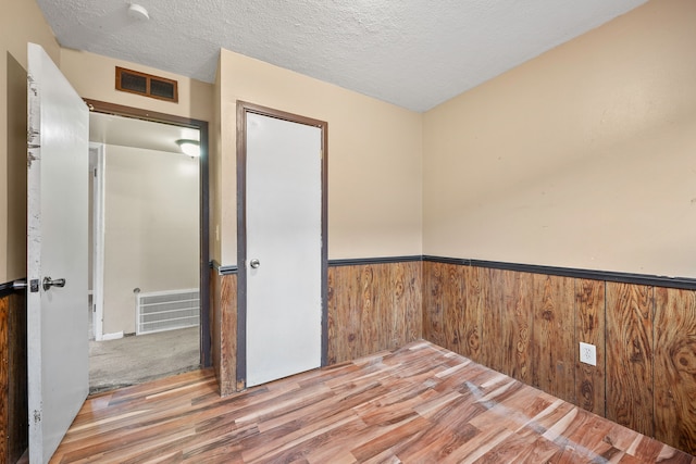 empty room featuring wooden walls, visible vents, a wainscoted wall, wood finished floors, and a textured ceiling